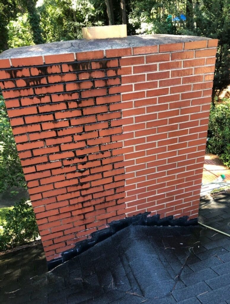 A brick chimney with the left side stained black and the right side clean, showing a clear contrast after partial cleaning.