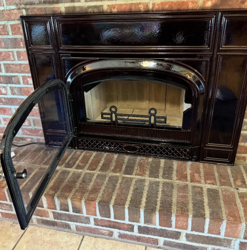 Fireplaces & Inserts: A black metal fireplace insert with an open glass door is set into a brick hearth and surrounded by a brick wall.